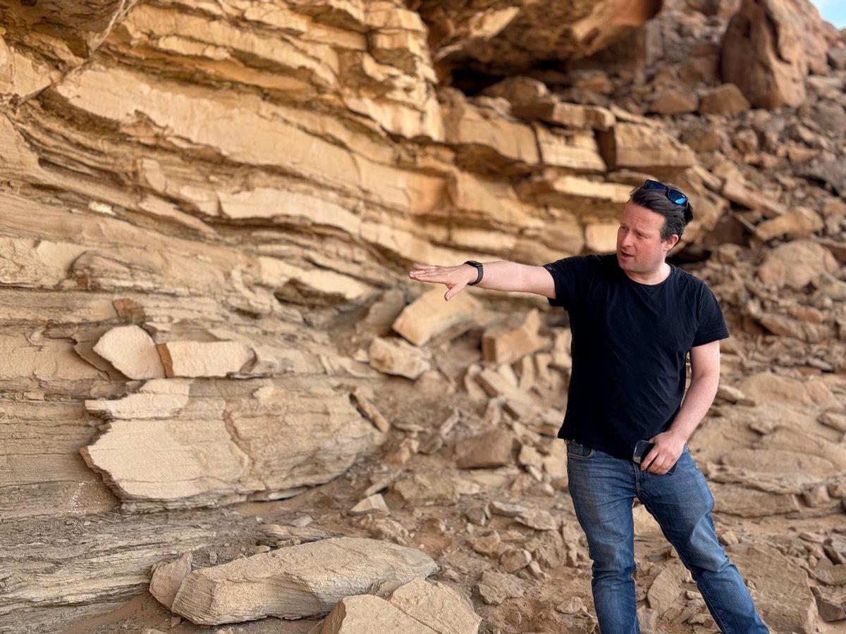 Paul Lyon at an outcrop, pointing out the bedding and fault geometry in a layered sandstone cliff